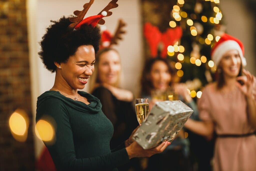 African American Woman Bringing Gift During Gathered At Home To Celebrate Christmas With Friends